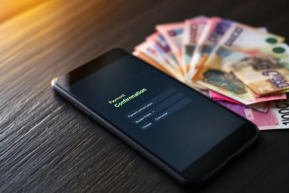 Billetes de pesos chilenos junto a un teléfono con una confirmación de pago