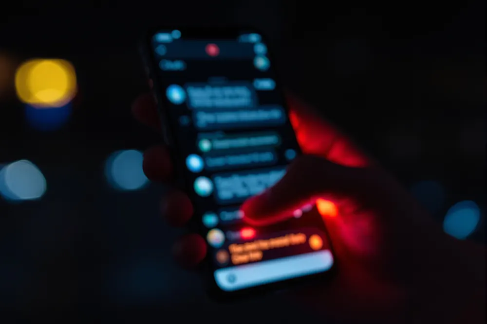 Mano sosteniendo un teléfono con un chat sospechoso y luz roja de advertencia